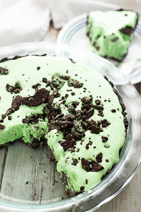 Overhead view of a Grasshopper pie with a slice missing, topped with Oreo crumbles in a glass pie dish