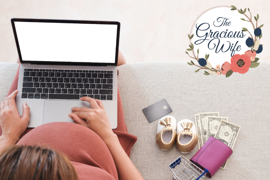 Pregnant mom sitting on a couch with a laptop on her lap next to baby shoes, wallet, credit card, and some cash