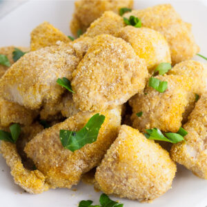 Stack of baked catfish nuggets on a small plate topped with fresh chopped parsley