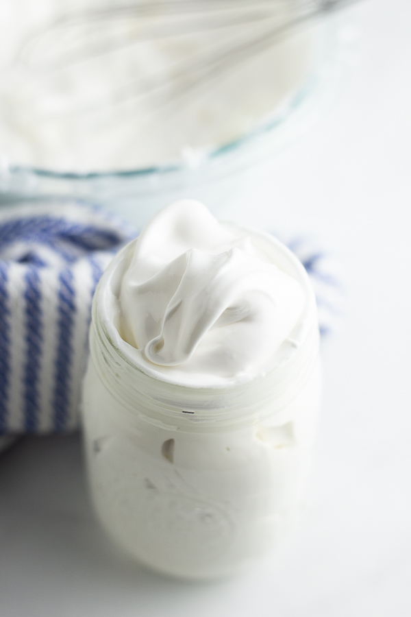 Homemade marshmallow fluff in a mason jar with a linen behind it.