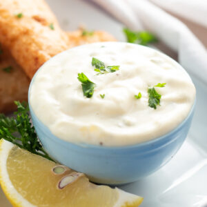 Small bowl filled with homemade tartar sauce and topped with fresh chopped parsley next to a lemon wedge and fried fish