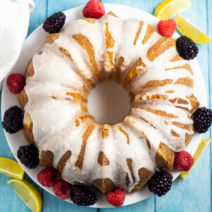 Overhead picture of a lemon buttermilk pound cake with lemon glaze drizzled on top next to fresh blackberries and raspberries and lemon wedges