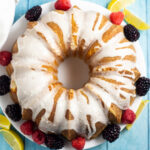 Overhead picture of a lemon buttermilk pound cake with lemon glaze drizzled on top next to fresh blackberries and raspberries and lemon wedges