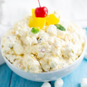 Side view of bowl of Pineapple Fluff topped with pineapple pieces and a cherry.