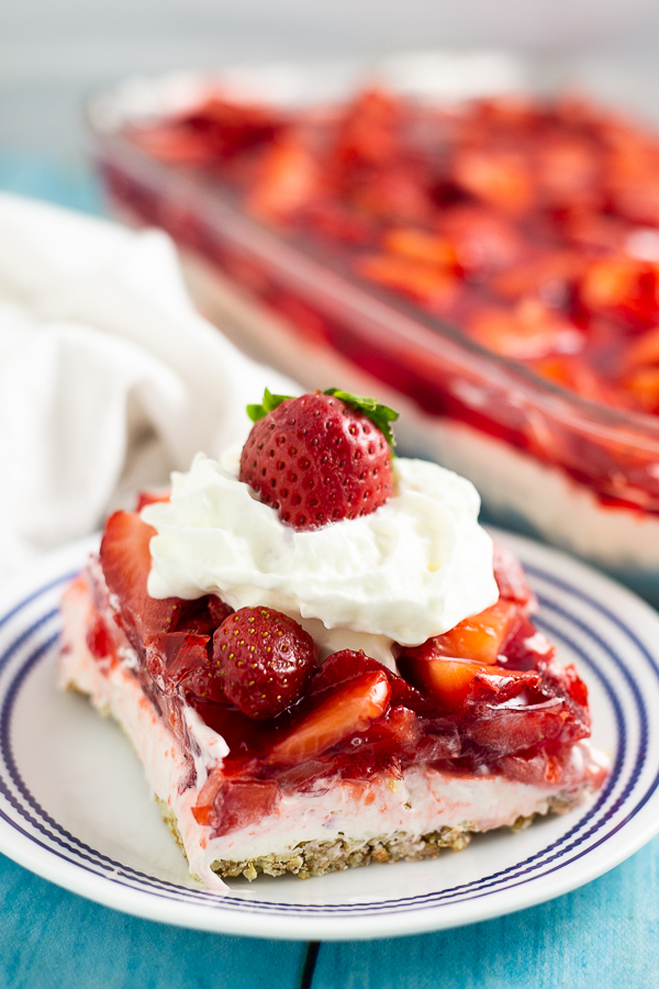 A slice of strawberry pretzel salad on a small plate topped with whipped cream and a fresh strawberry.