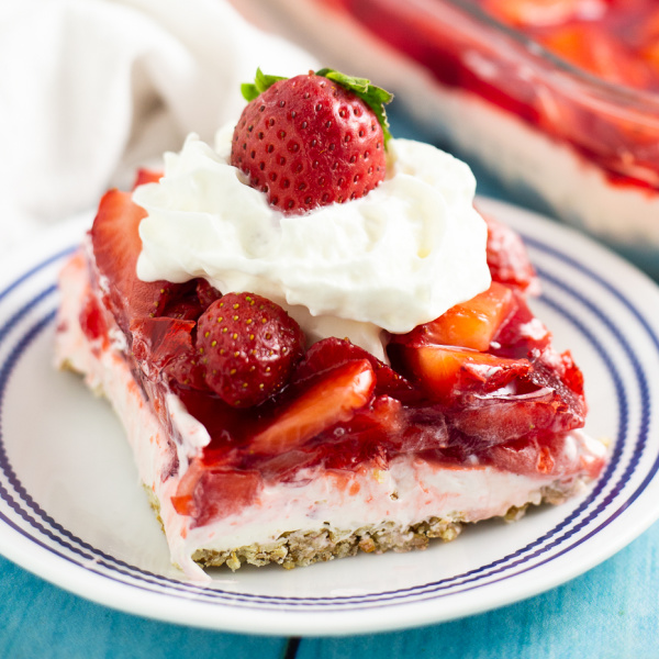A slice of strawberry pretzel salad on a small plate topped with whipped cream and a fresh strawberry.