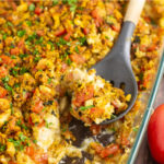 Casserole dish filled with bruschetta chicken bake with a spoonful missing and a wooden spoon in the dish.