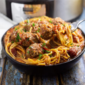 Crock Pot Spaghetti and Meatballs in a shallow bowl with a fork picking some spaghetti and a meatball with a slow cooker in the background