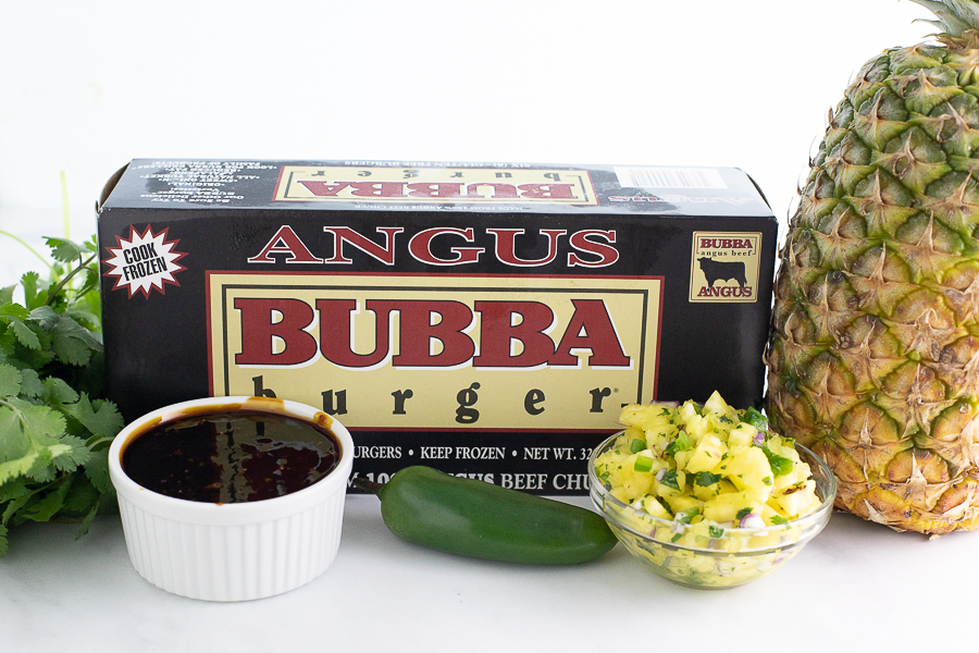 Aungus BUBBA Burger box on a marble counter top surrounded by fresh pineapple and cilantro, homemade bourbon teriyaki, and pineapple salsa