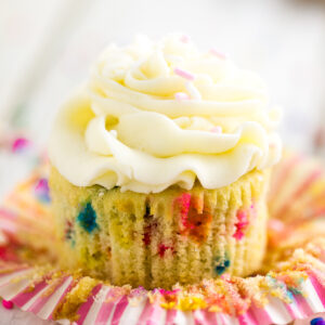 Unwrapped funfetti cupcake topped with buttercream surrounded by rainbow sprinkles