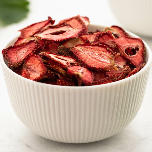 Bowl full of dried strawberries with strawberry leaves in the background