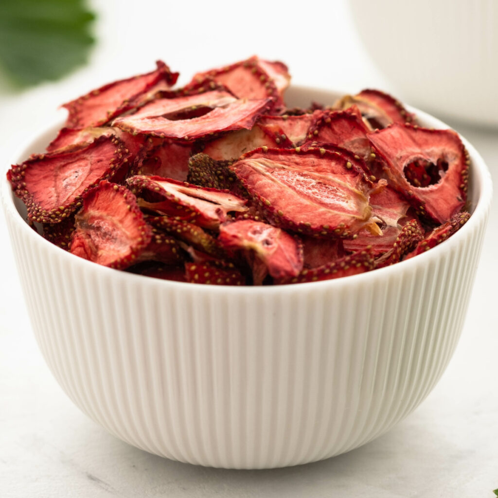 Bowl full of dried strawberries with strawberry leaves in the background