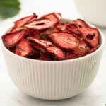 Bowl full of dried strawberries with strawberry leaves in the background