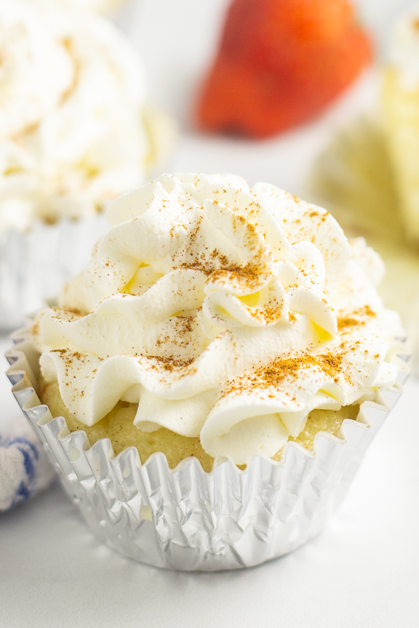 Close up of a cupcake in a foil wrapper topped with whipped mascarpone frosting and a sprinkle of cinnamon