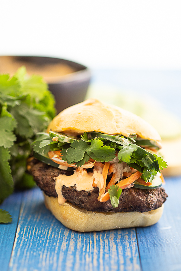 Side view of a fully topped banh mi burger with a little drizzle of spicy mayo running down the side.