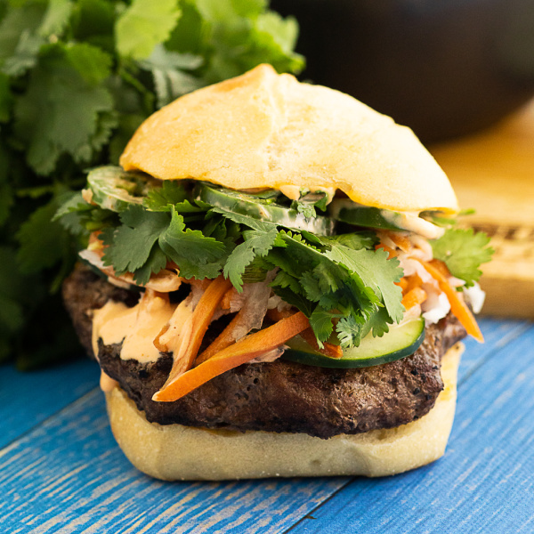 Front view of a banh mi burger piled high with toppings and spicy mayo