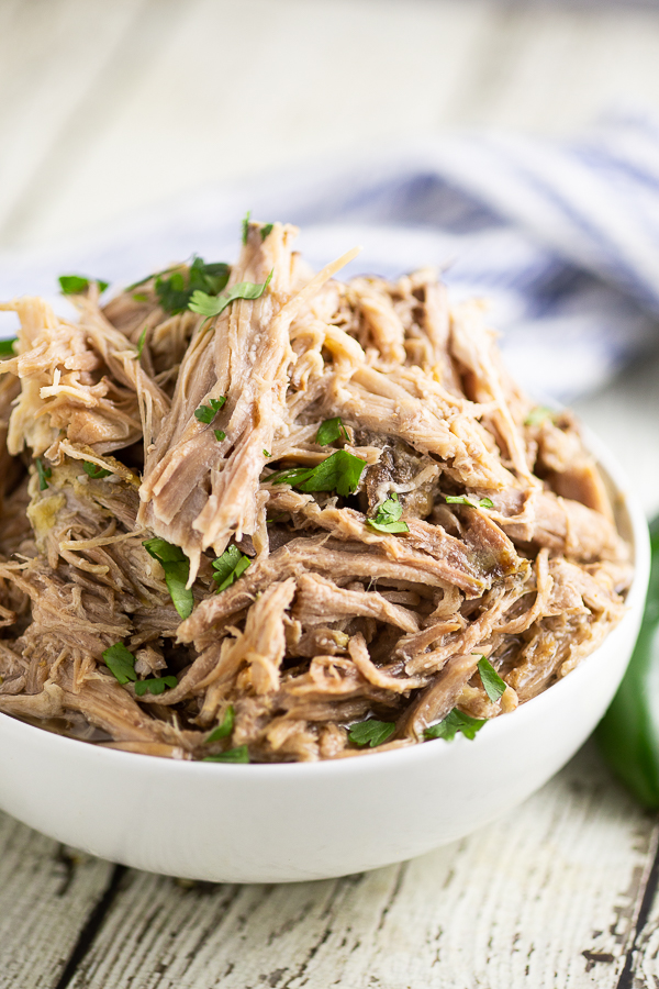 Close up view of a bowl filled with slow cooker Chipotle carnitas, topped with chopped fresh cilantro with a linen behind it.