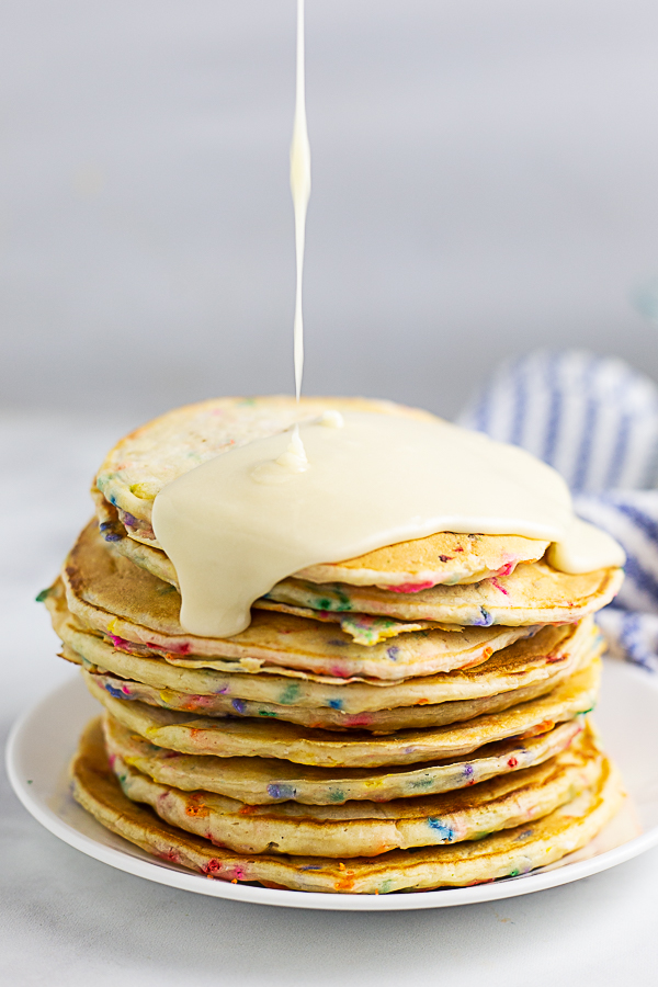 A stack of funfetti pancakes on a small plate being drizzled with vanilla glaze