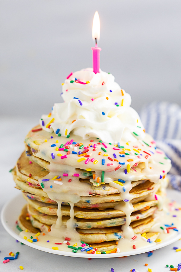 Funfetti pancakes drizzled with a vanilla glaze, topped with whipped cream, rainbow sprinkles, and a candle
