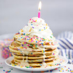 Funfetti pancakes drizzled with a vanilla glaze, topped with whipped cream, rainbow sprinkles, and a candle
