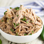 A bowl filled with slow cooker Chipotle carnitas, topped with chopped fresh cilantro