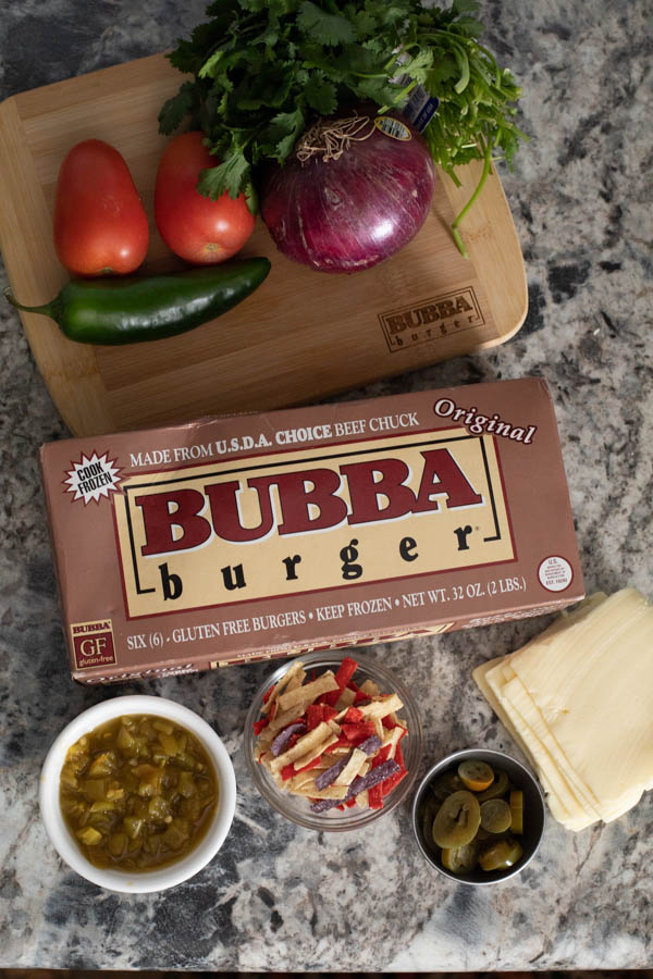 BUBBA burger package on a counter with tomatoes, jalapeno, onion, cilantro, green chiles, tortilla strips, and white American cheese.