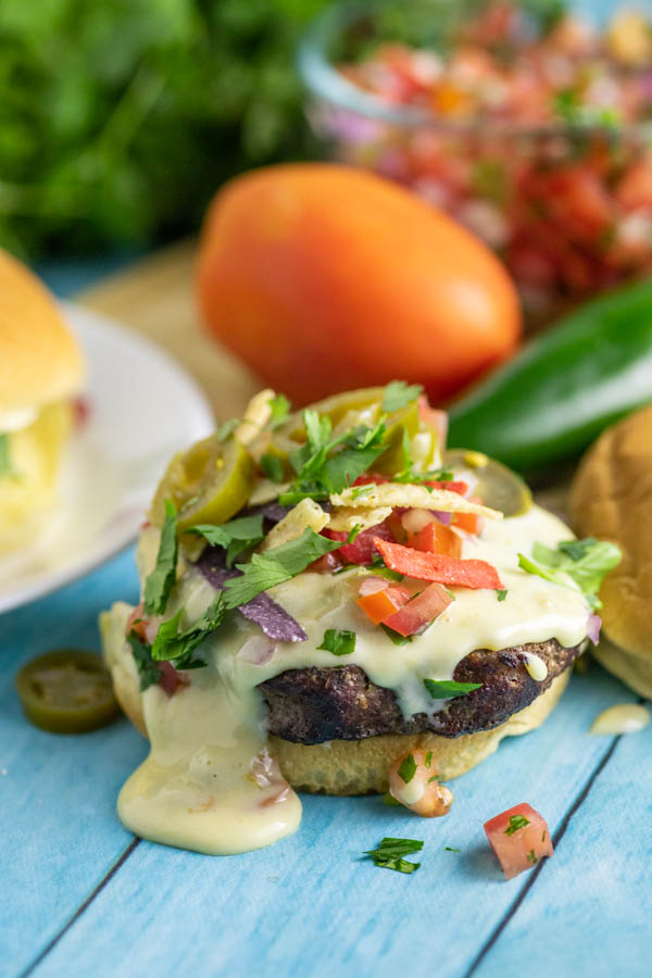 Open face nacho burger topped with queso, pico de gallo, pickled jalapenos, and tortilla strips
