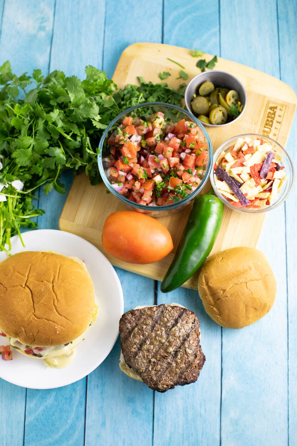 Nacho burger ingredients spread out on a cutting board and a blue wood background