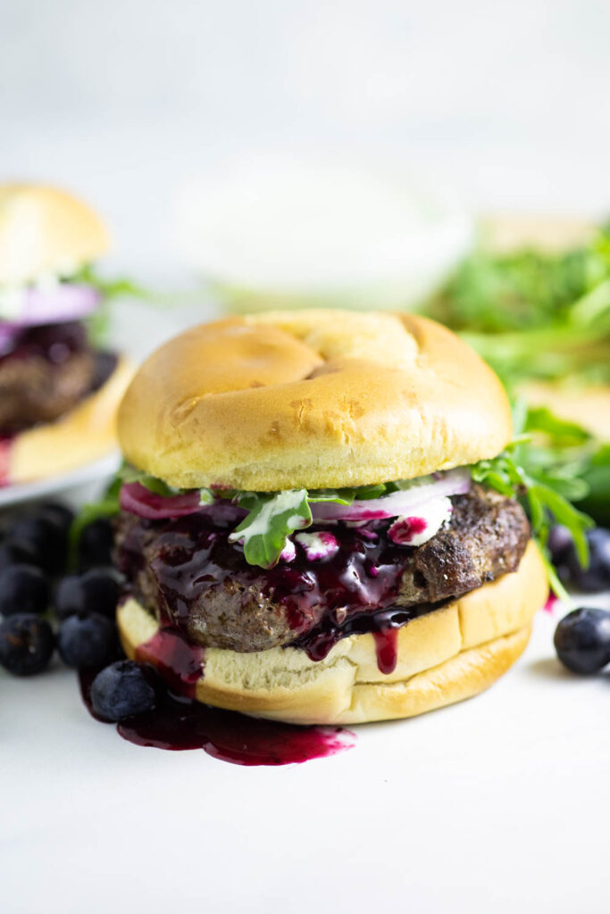 Front view of a spicy blueberry burger with blueberry sauce running down with fresh arugula in the backgrounf