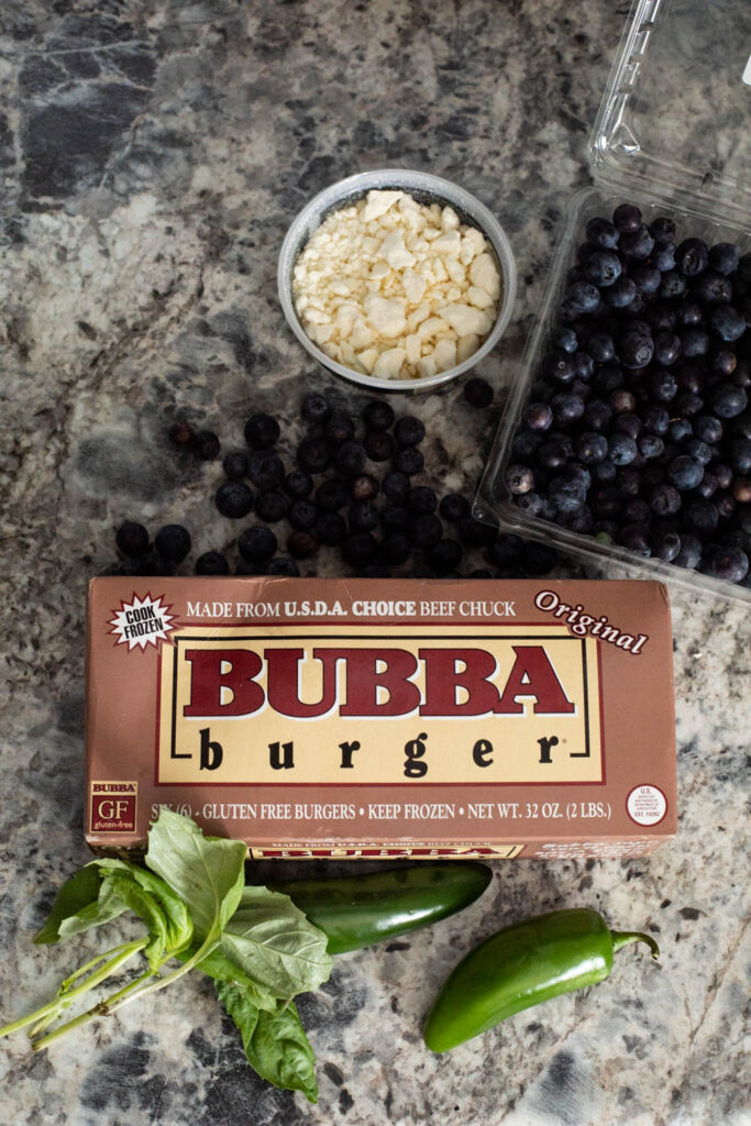 Ingredients to make a spicy blueberry burger, including fresh blueberries, feta cheese, basil, jalapenos, and burgers