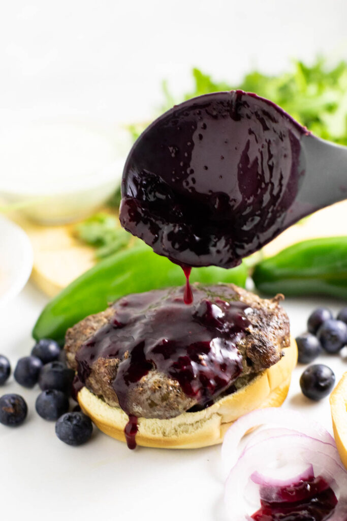 Blueberry Sauce being drizzled onto a burger with jalapenos and blueberries surrounding it.