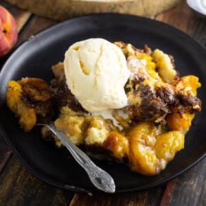 Peach cobbler on a plate topped with ice cream with a spoon