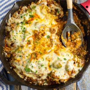 Unstuffed peppers covered in melted mozzarella in a cast iron skillet with a spoon in the middle