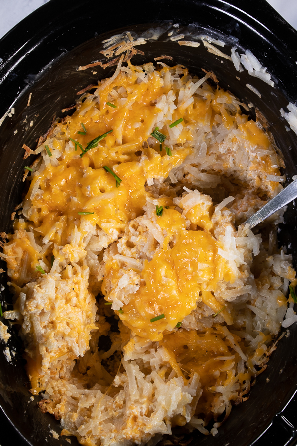 Slow cooker full of Crock Pot Hash Brown Casserole with a spoon in the middle taking a scoop Pot