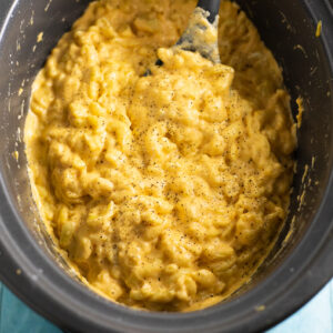 Mac and cheese in a crockpot topped with fresh cracked black pepper with a spoon sticking out.