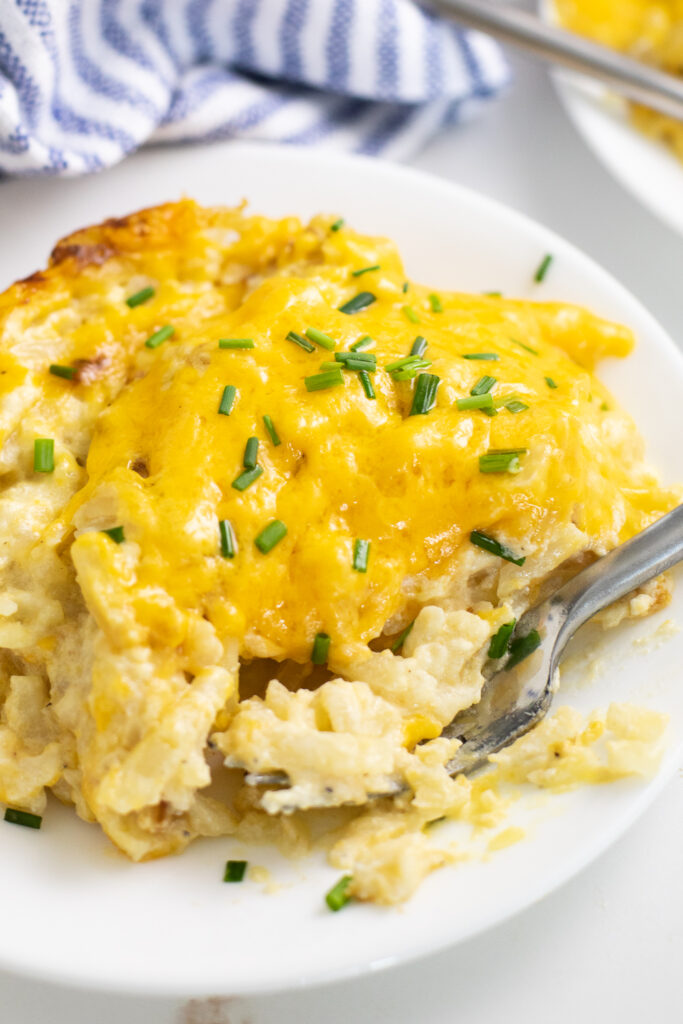 Crock pot hash brown casserole topped with fresh chopped chives on a small plate with a fork in it.