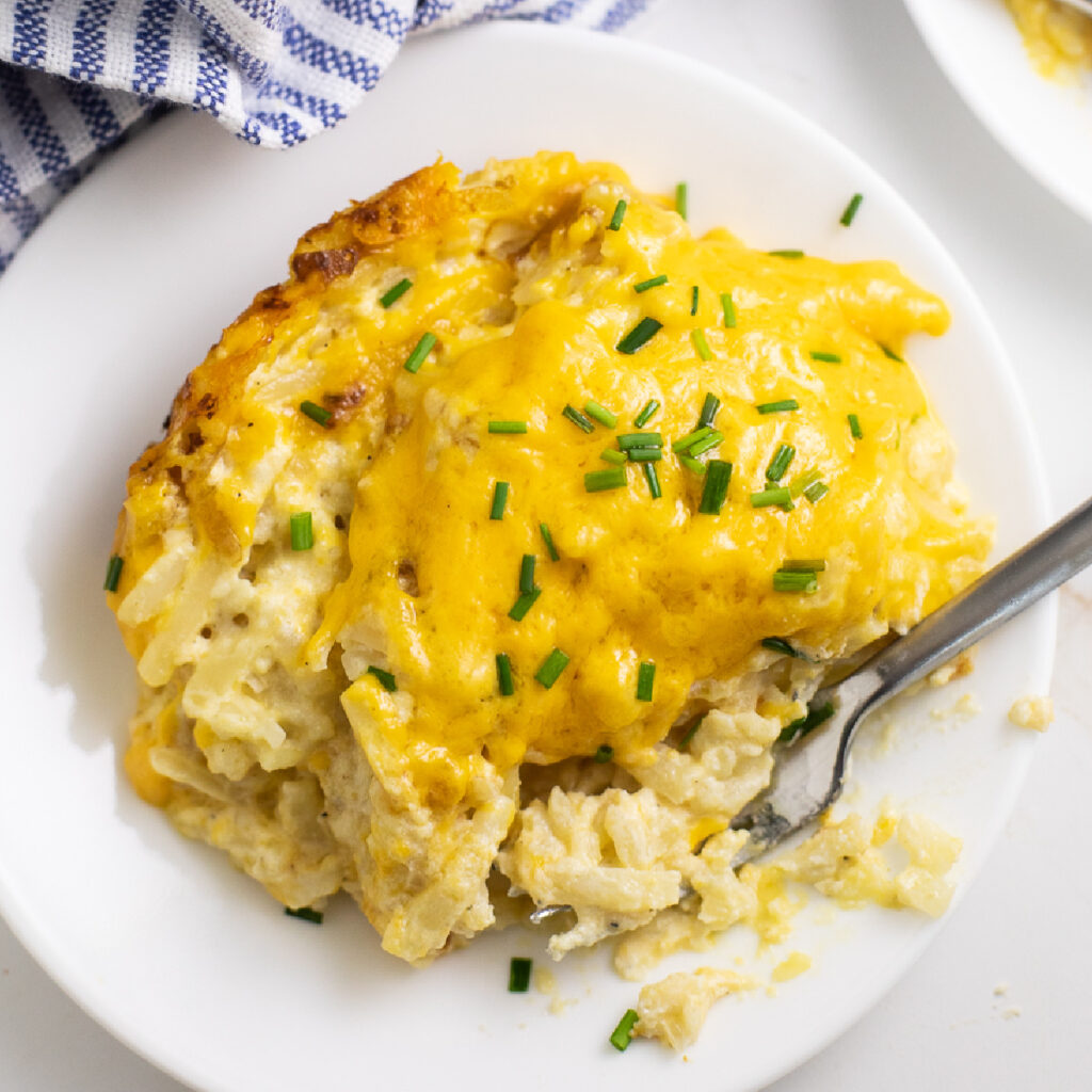 Crock pot hash brown casserole topped with fresh chopped chives on a small plate with a fork in it.