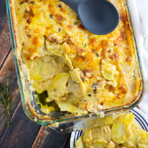 Casserole dish filled with scalloped potatoes with a scoop taken out and a wooden spoon on top.
