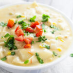 Chicken tortilla chowder in a white bowl topped with fresh chopped tomatoes and cilantro.