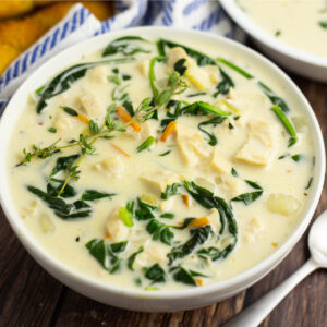 Chicken Gnocchi Soup in a white bowl with a rustic wood background and breadsticks in a white and blue striped linen behind it.