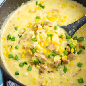 Close up photo of cheesy ham and corn chowder in a cast iron dutch oven with a ladle in the middle.