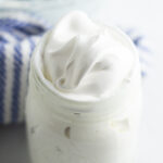 Homemade marshmallow fluff in a mason jar with a linen behind it.