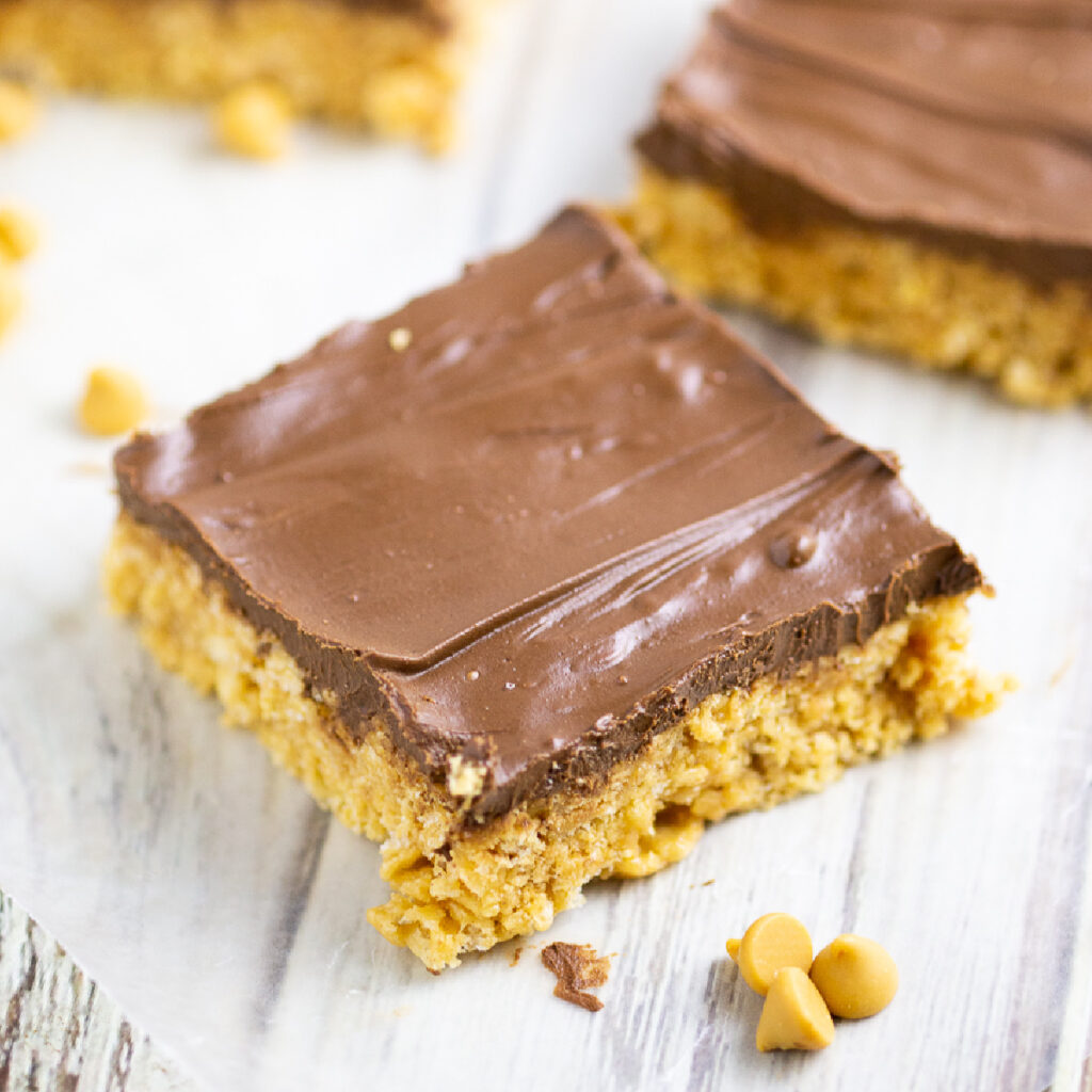 Scotcheroo bar sitting on a piece of parchment paper on a rustic wood background with butterscotch chips