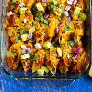 Casserole dish filled with taco stuffed shells topped with fresh avocado, red onion, and cilantro.