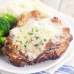 Bacon Swiss pork chop on a small plate next to broccoli and mashed potatoes.
