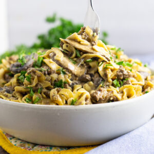Ground beef stroganoff in a shallow bowl with a fork taking a bite off the top.