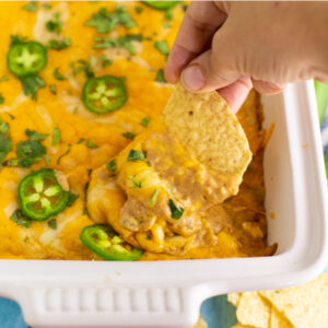 Texas trash dip in a white ceramic casserole dish topped with fresh jalapeno slices and chopped cilantro with a tortilla chip dipping in.
