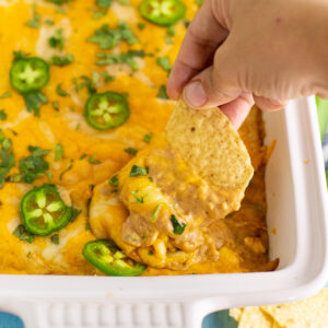 Texas trash dip in a white ceramic casserole dish topped with fresh jalapeno slices and chopped cilantro with a tortilla chip dipping in.