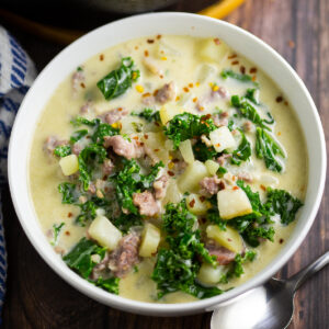 Bowl full of Zuppa Toscana next to a spoon and large pot of soup