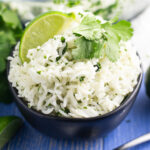 White chipotle lime rice garnished with a fresh lime wedge and sprig of cilantro in a black bowl on a blue wood background